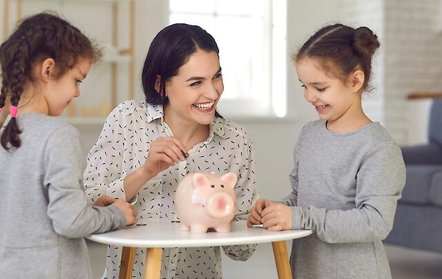 mother showing daughters how to save money with a piggy bank